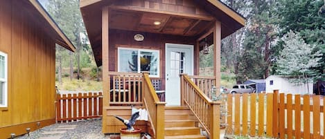 A wooden cabin with a porch, a staircase, and a fenced yard.