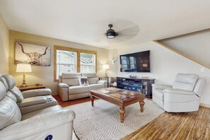 Ein Wohnzimmer mit Sofa, Sessel, Couchtisch und einem an der Wand befestigten Flachbildfernseher.