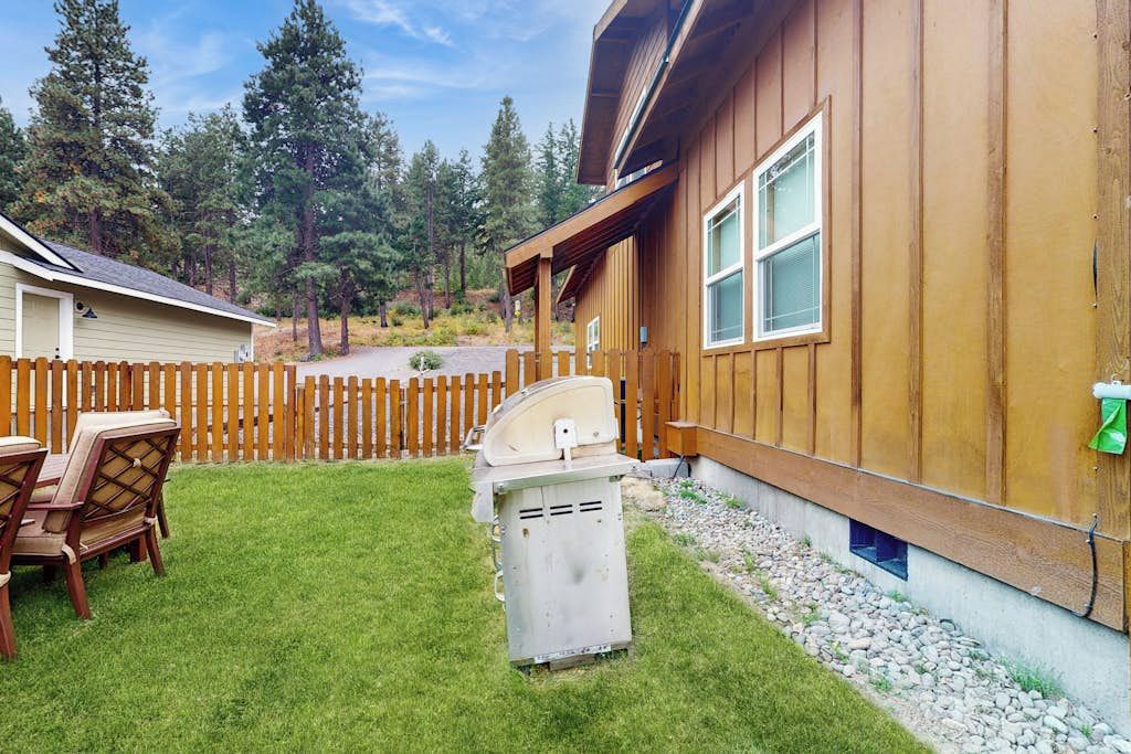 A wooden cabin with a covered patio, a grill, and a fenced yard.
