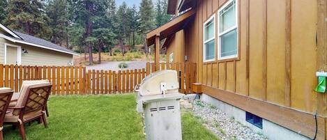 A wooden cabin with a covered patio, a grill, and a fenced yard.