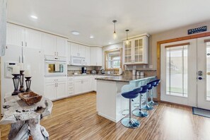 A modern kitchen with white cabinets, a central island with bar stools, and a welcome sign. - 2 BR Lakefront home with kayak and paddle boat (Cle Elum)