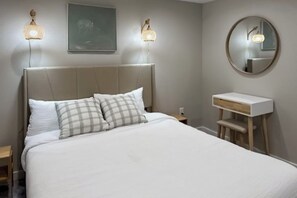 A bedroom with a bed, bedside tables, a nightstand, a bedside lamp, a mirror, and a wall-mounted light fixture. - Two BR duplex with wifi, Washer Dryer & convenient location (Seattle)