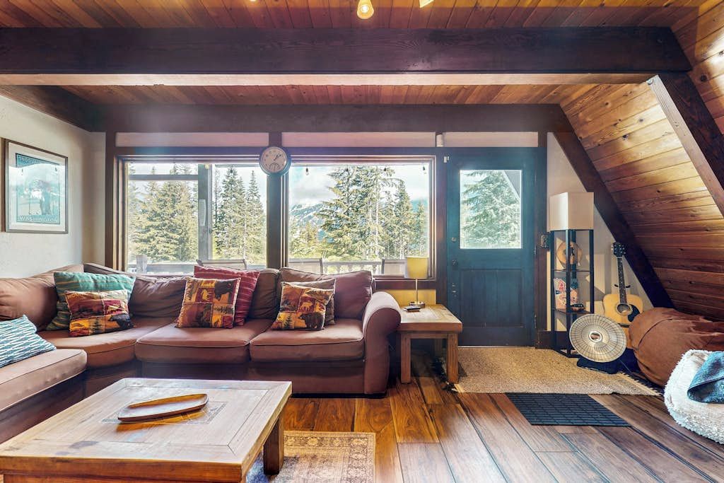 Ein gemütliches Wohnzimmer mit einer braunen Ledersofa, einem Holztisch und einem großen Fenster mit Blick auf Bäume.