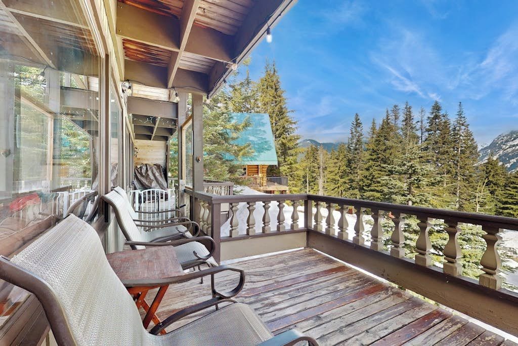 A wooden deck with outdoor furniture, a railing, and a view of trees and mountains.