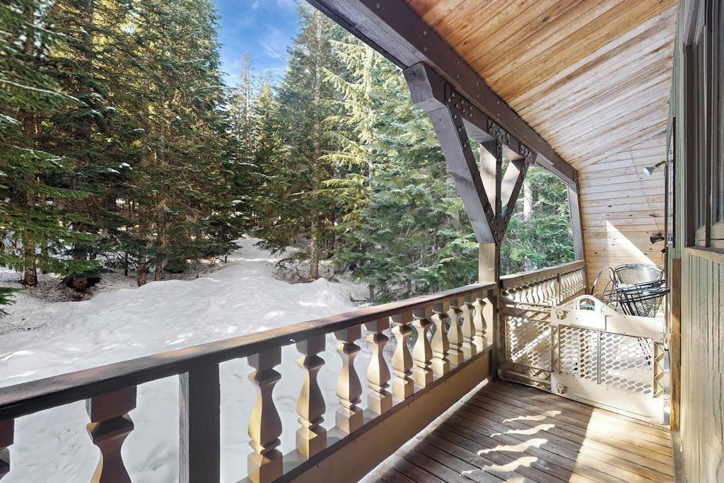A wooden deck with a railing overlooking a snowy landscape with trees.
