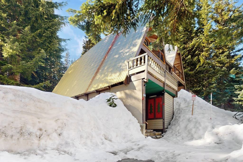 A snow-covered building with a red door, surrounded by trees and a large pile of snow.