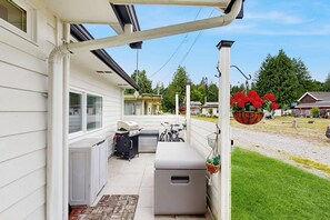 Ett takförsett utomhusområde med en grill, ett litet kylskåp och en hängande blomkorg.