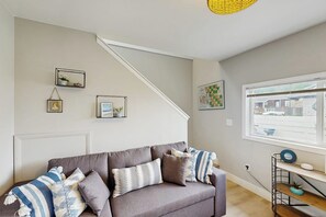 A living room with a grey sofa, a staircase, and a window with a view of the street. - 2BR with amazing views, firepit (Bow)