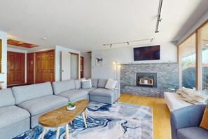 Een moderne woonkamer met een hoekbank, een open haard en een groot raam.