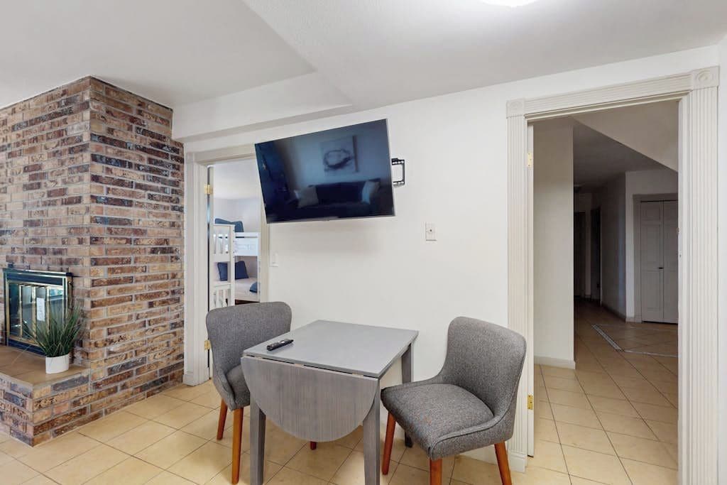 Una habitación con chimenea de ladrillo, un televisor de pantalla plana en la pared y una pequeña mesa con dos sillas.