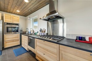 A modern kitchen with wooden cabinets, stainless steel appliances, and a black countertop. - 2BR oceanfront house with beach access (Westport)