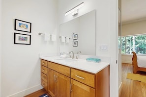 A bathroom with a double sink, wooden cabinets, a large mirror, and framed pictures on the wall. - Charming 1BR Retreat - Patio - Golf Nearby - WIFI (Bainbridge Island)
