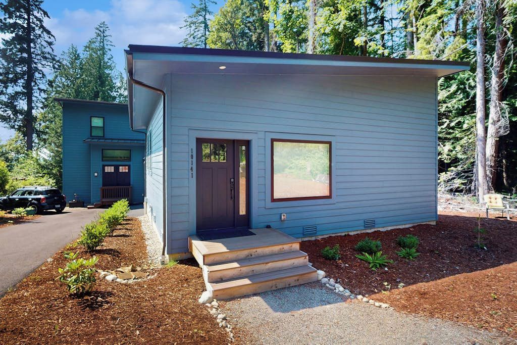 A modern single-story house with a dark front door, a small window, and a set of wooden steps leading to the entrance.