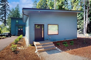 A modern single-story house with a dark front door, a small window, and a set of wooden steps leading to the entrance. - Charming 1BR Retreat - Patio - Golf Nearby - WIFI (Bainbridge Island)