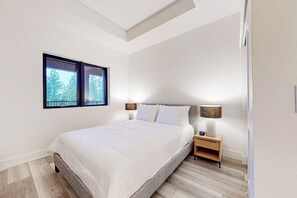 Une chambre à coucher avec un lit, deux lampes de chevet, une table de chevet et une fenêtre donnant sur des arbres.