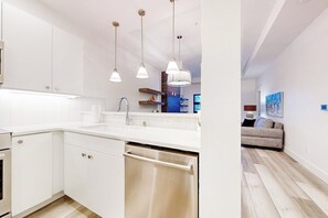 Une cuisine moderne avec des meubles blancs, des appareils en acier inoxydable et des luminaires suspendus.