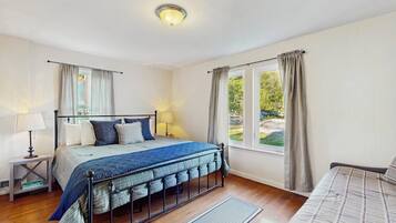 Une chambre à coucher avec un lit, des tables de chevet, une fenêtre avec des rideaux et une vue sur la verdure à l’extérieur.