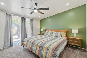 Een slaapkamer met een bed, twee nachtkastjes, een plafondventilator en uitzicht door een raam.