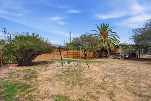 A backyard with a swing set, a palm tree, and a brick wall. - *New* Close to Uof A & Downtown~Sleeps7~Casa Elida (Tucson)