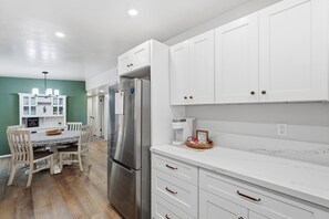 A modern kitchen with white cabinetry, a stainless steel refrigerator, a dining table with chairs, and a coffee machine. - *New* Close to Uof A & Downtown~Sleeps7~Casa Elida (Tucson)