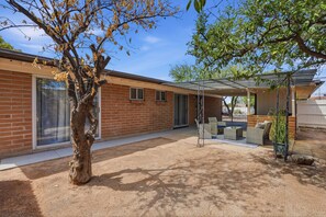 A covered patio area with outdoor furniture, a brick building, and a tree with yellowing leaves. - *New* Close to Uof A & Downtown~Sleeps7~Casa Elida (Tucson)