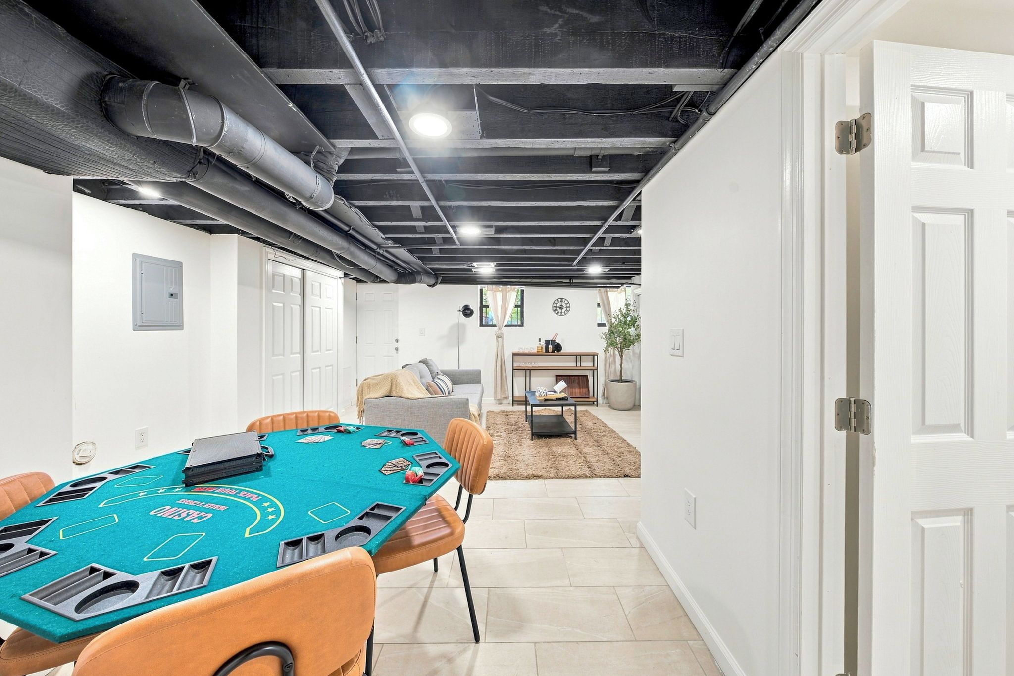 A room with a blackjack table, chairs, a sofa, a small table with a plant, and a door.