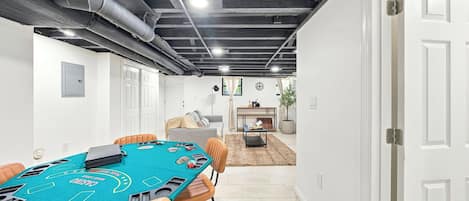 A room with a blackjack table, chairs, a sofa, a small table with a plant, and a door.
