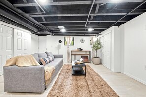 Ein Wohnzimmer mit einem grauen Sofa, einem schwarzen Couchtisch, einem braunen Teppich, einem Kamin und einer Topfpflanze.