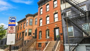 A row of red brick buildings with fire escapes, a bus stop sign, and a no parking sign.