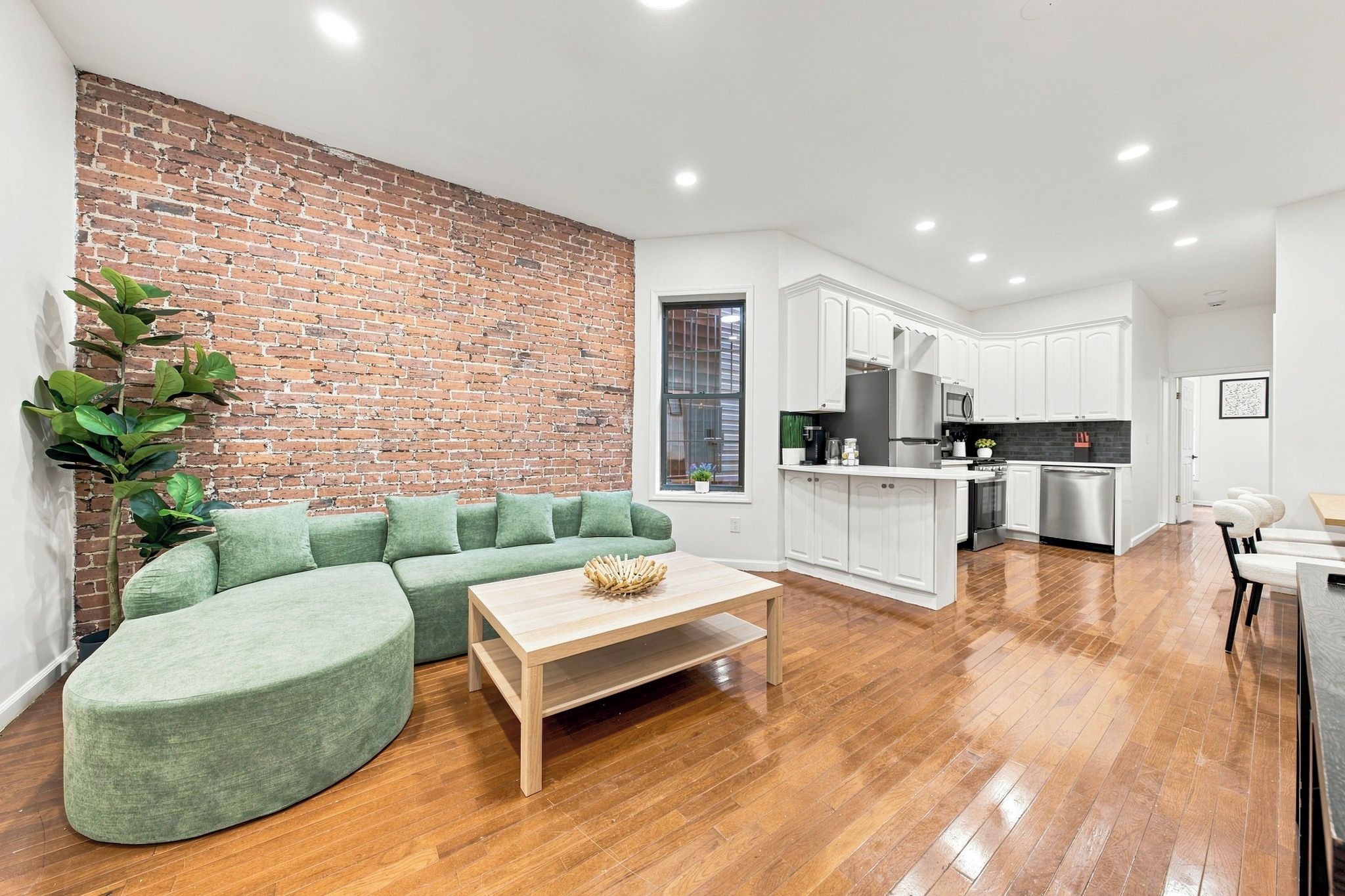 Un salon moderne avec un canapé d’angle vert, une table basse en bois et un mur décoratif en briques.