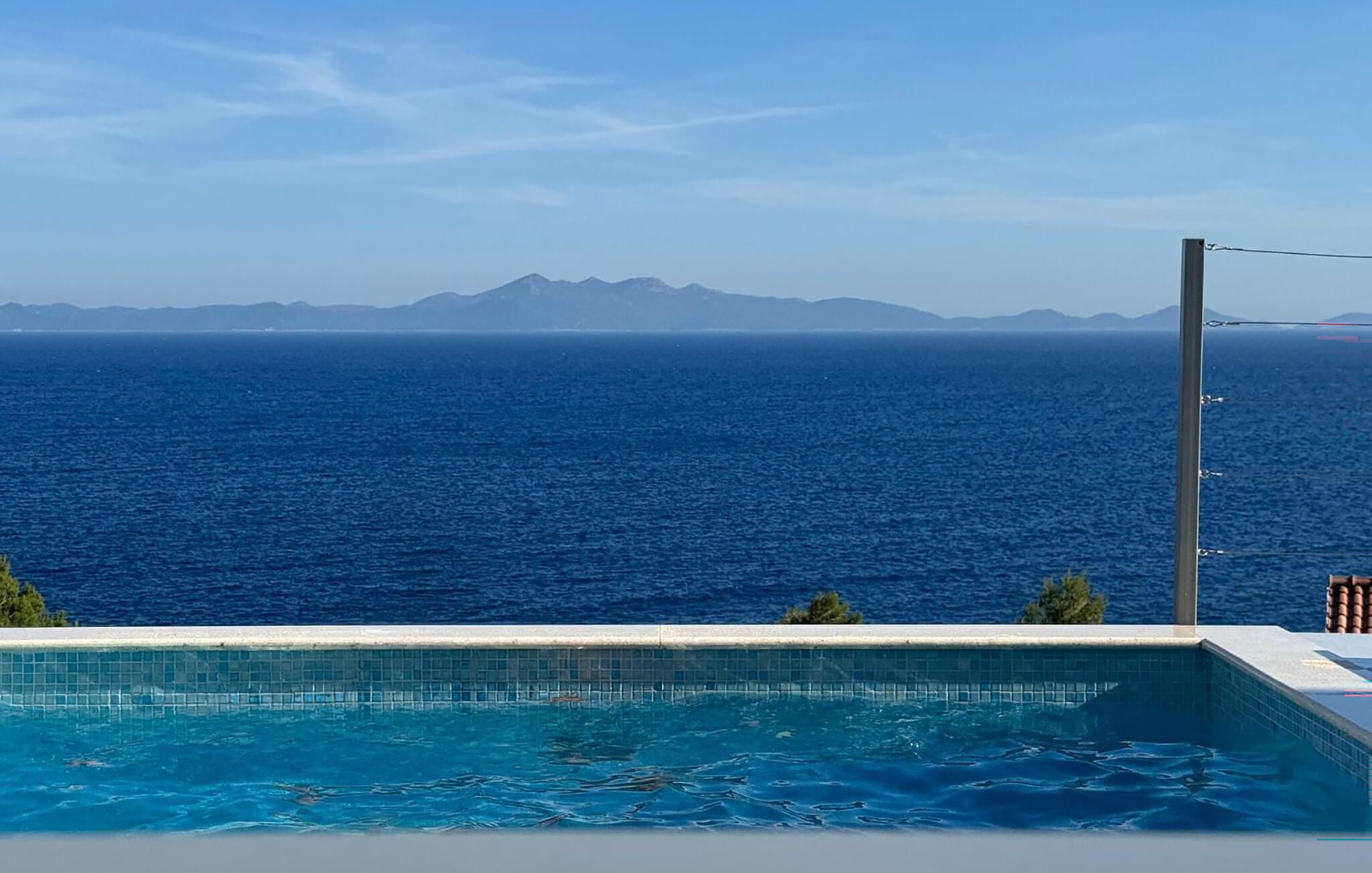 En swimmingpool med utsikt över havet och avlägsna berg.