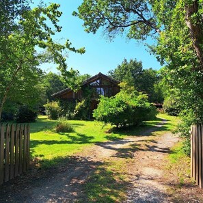 Eine Holzhütte, umgeben von üppigem Grün, mit einem Kiesweg, der zu ihr führt.