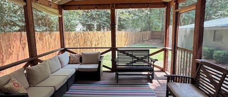 Een overdekt terras met een bank, zitplaatsen en een kleurrijk gestreept tapijt.