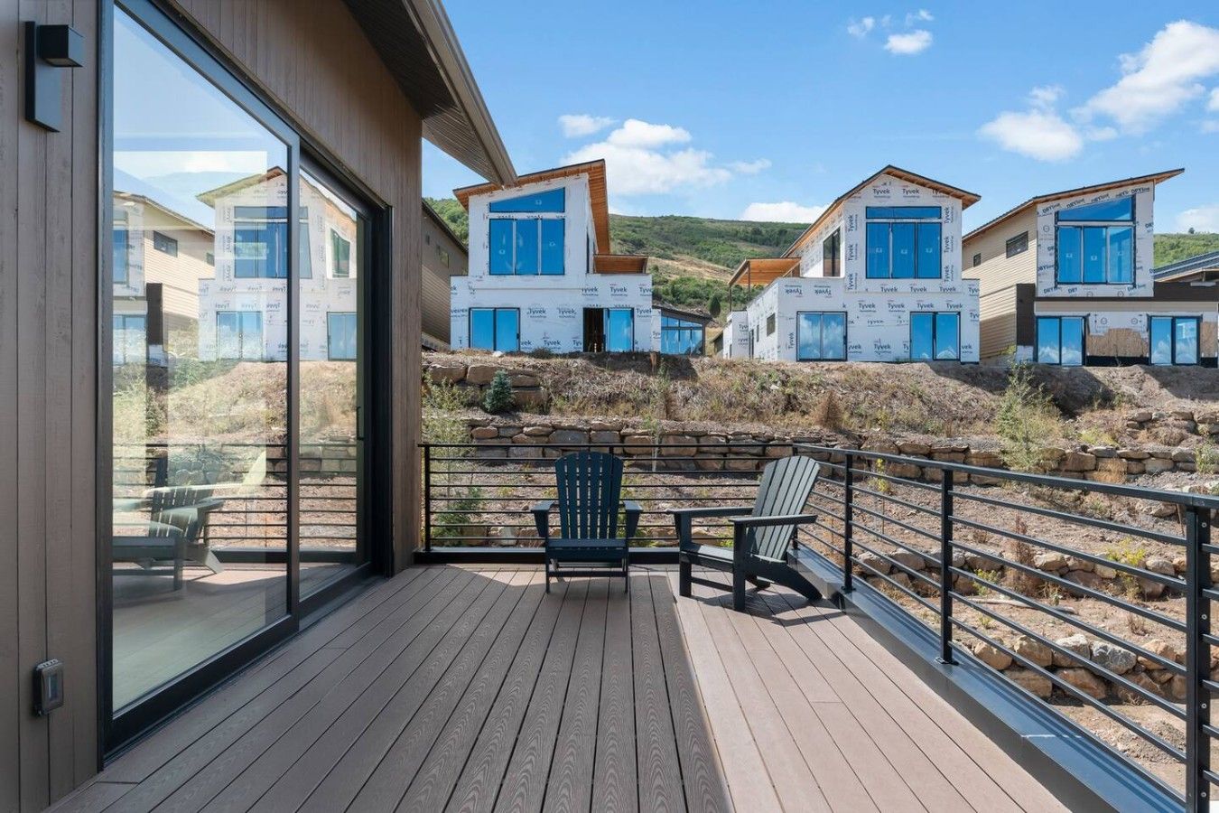 Eine Holzterrasse mit Geländer, die einen Hügel mit modernen Häusern im Bau überblickt.