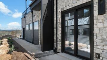 A modern two-story house with stone exterior walls, large sliding glass doors, and a balcony.