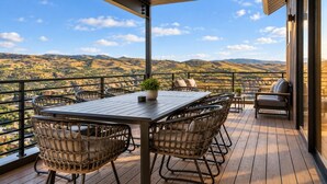 A wooden deck with a table and chairs, overlooking a mountainous landscape. - Ski & Lake Retreat | Golf Sim + Sauna + Firepit (Daniel)