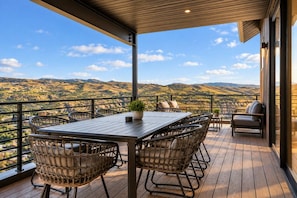 A wooden deck with a table and chairs, overlooking a mountainous landscape. - Ski & Lake Retreat | Golf Sim + Sauna + Firepit (Daniel)