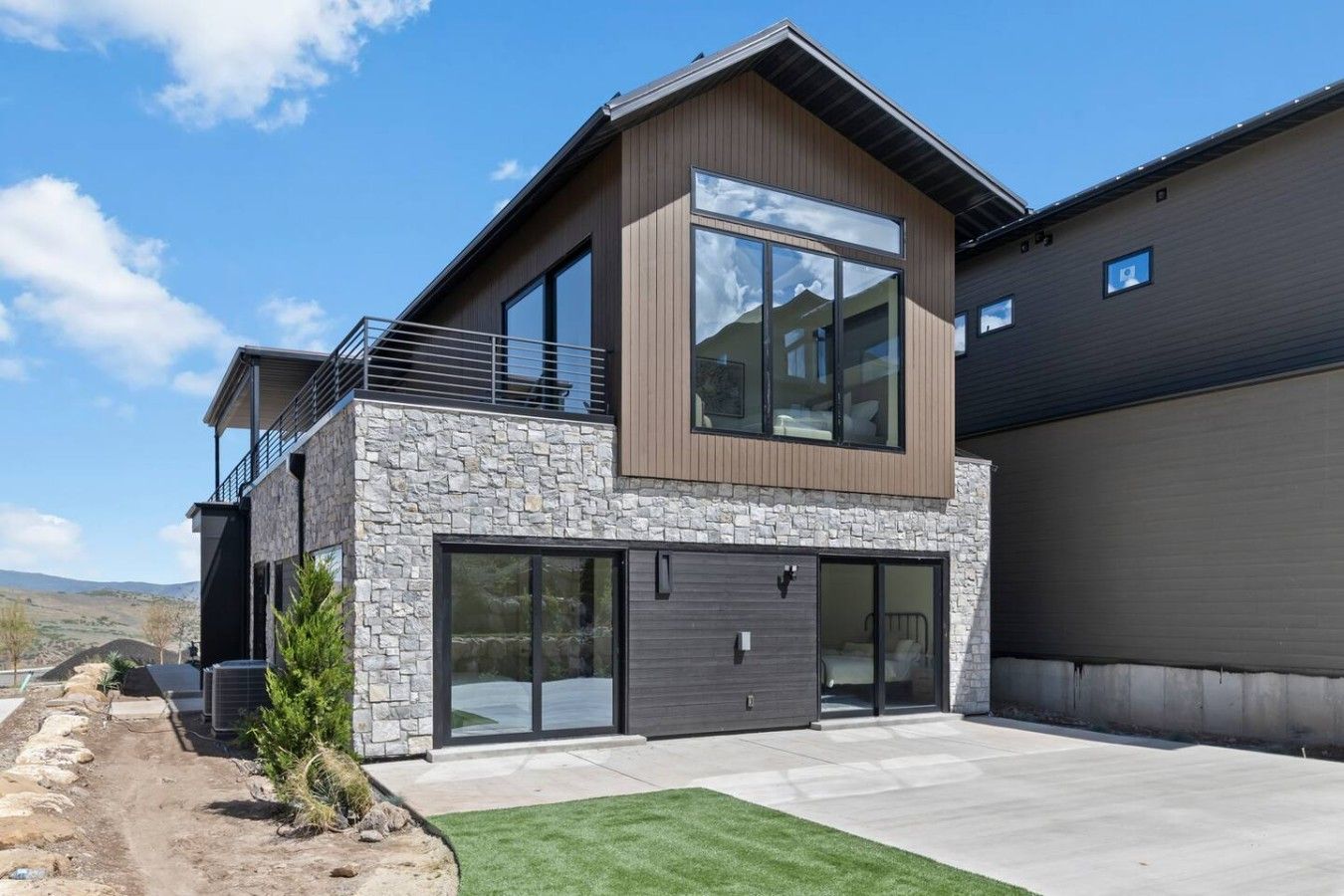 Une maison moderne à deux étages, dotée d’une façade en pierre, de grandes fenêtres et d’un garage.
