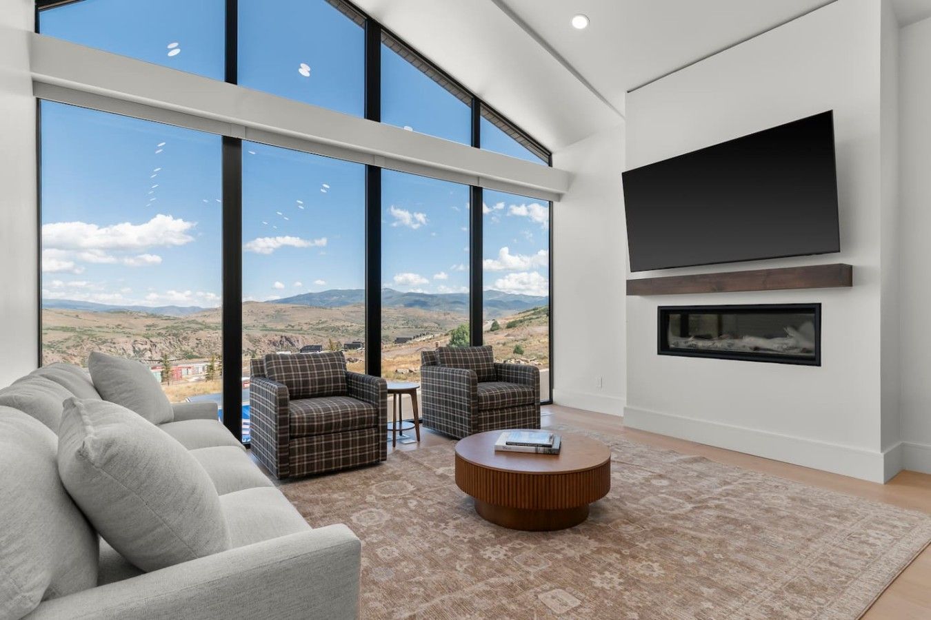 A modern living room with large windows, a flat-screen TV, and a fireplace.