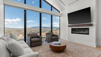 A modern living room with large windows, a flat-screen TV, and a fireplace.