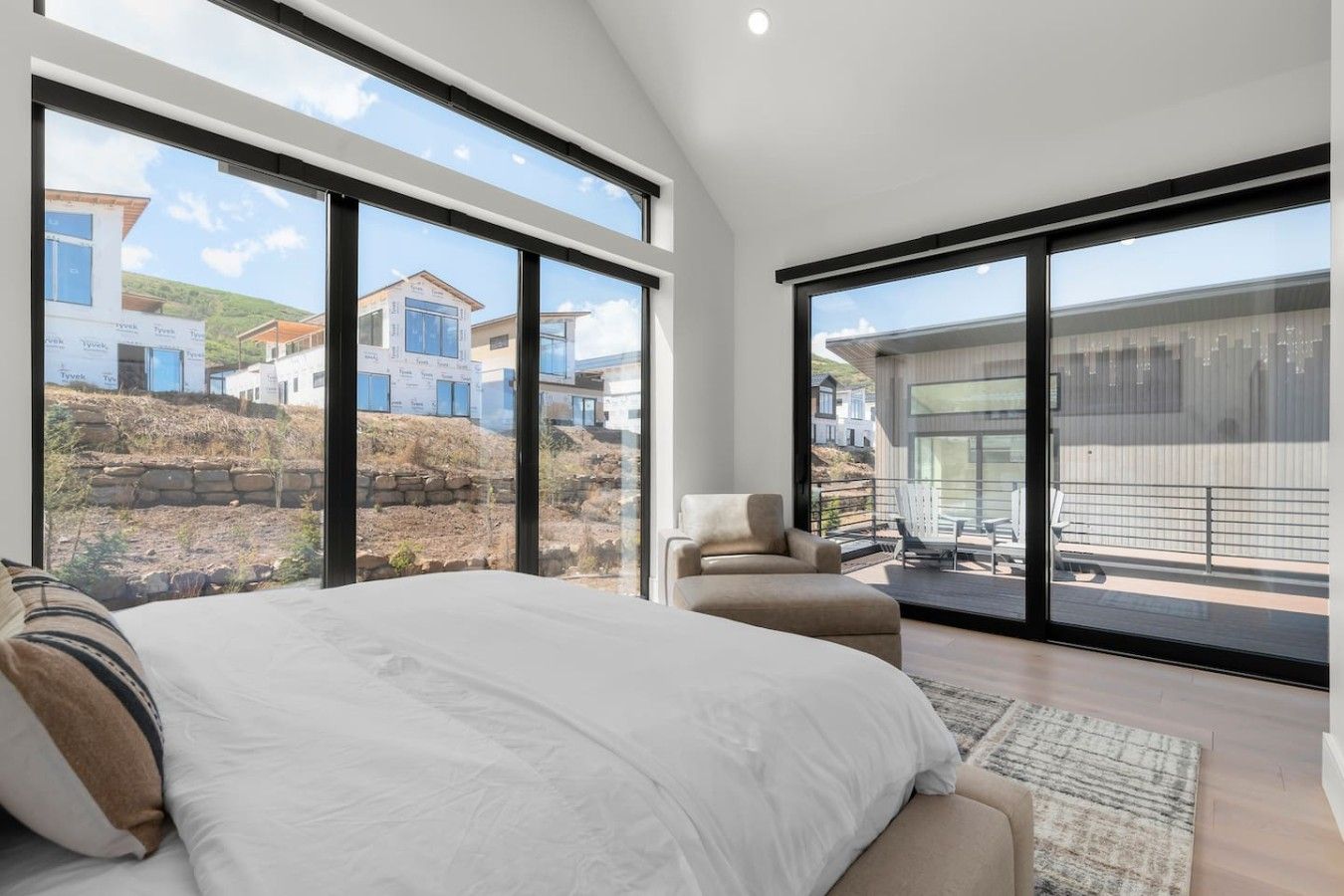 A bedroom with a large bed, a sofa, and a balcony with a view of houses and a construction site.