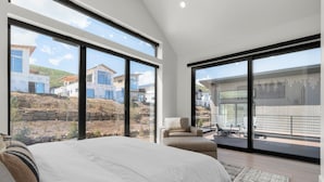 A bedroom with a large bed, a sofa, and a balcony with a view of houses and a construction site. - Ski & Lake Retreat | Golf Sim + Sauna + Firepit (Daniel)