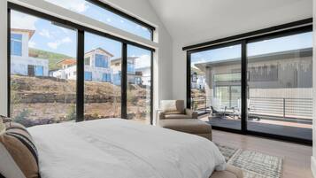 A bedroom with a large bed, a sofa, and a balcony with a view of houses and a construction site.