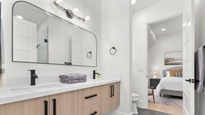 A modern bathroom with a large mirror, vanity, and a shower area. - Ski & Lake Retreat | Golf Sim + Sauna + Firepit (Daniel)