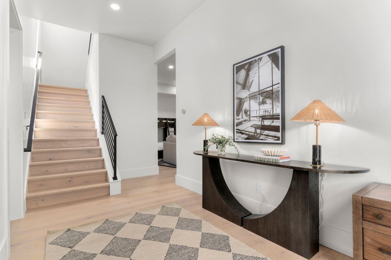 A modern interior with a staircase, a console table with lamps, and a framed picture on the wall.