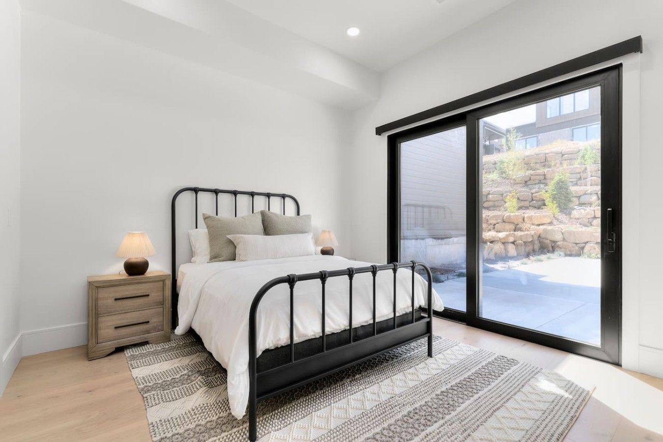 A bedroom with a bed, bedside tables, and a view through a sliding glass door.