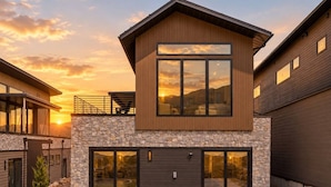 A modern two-story house with a stone facade, large windows, and a garage. - Ski & Lake Retreat | Golf Sim + Sauna + Firepit (Daniel)