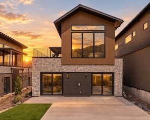 A modern two-story house with a stone facade, large windows, and a garage. - Ski & Lake Retreat | Golf Sim + Sauna + Firepit (Daniel)