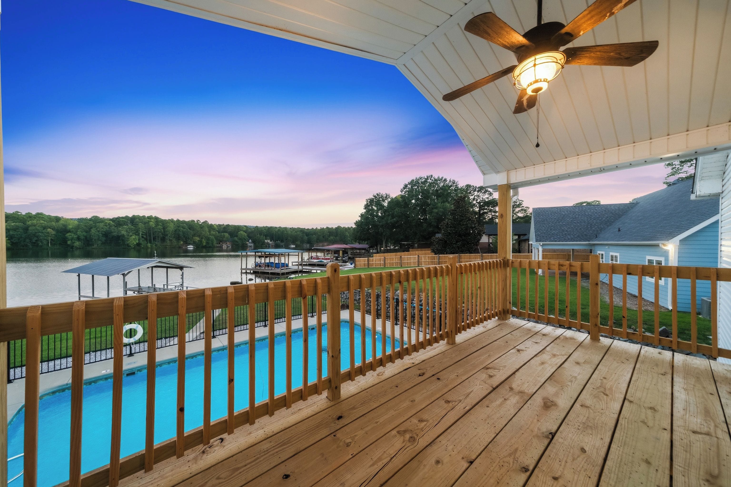 A wooden deck with a pool, overlooking a lake with boats and a dock.