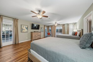 Ein Schlafzimmer mit einem großen Bett, einem Deckenventilator, einem Fernseher und Blick ins Freie.